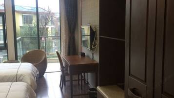 A hotel room with a bed, a desk, a chair, a television, and a window with a view of buildings outside.