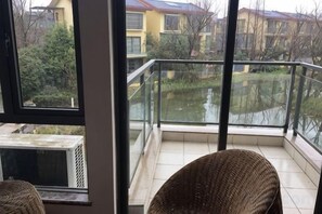 En balkon med gelænder af glas, en fletstol og udsigt over et boligområde.