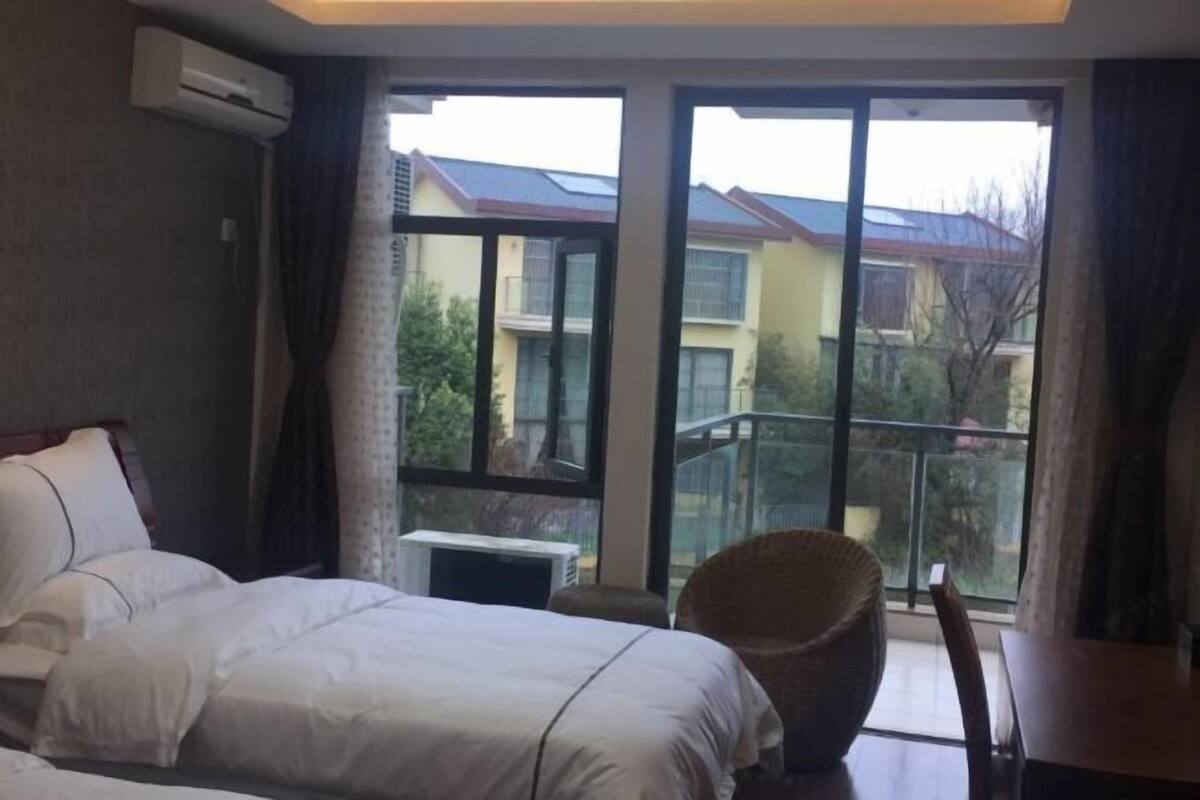 A hotel room with a bed, a chair, a table, and a large window offering a view of neighboring buildings.