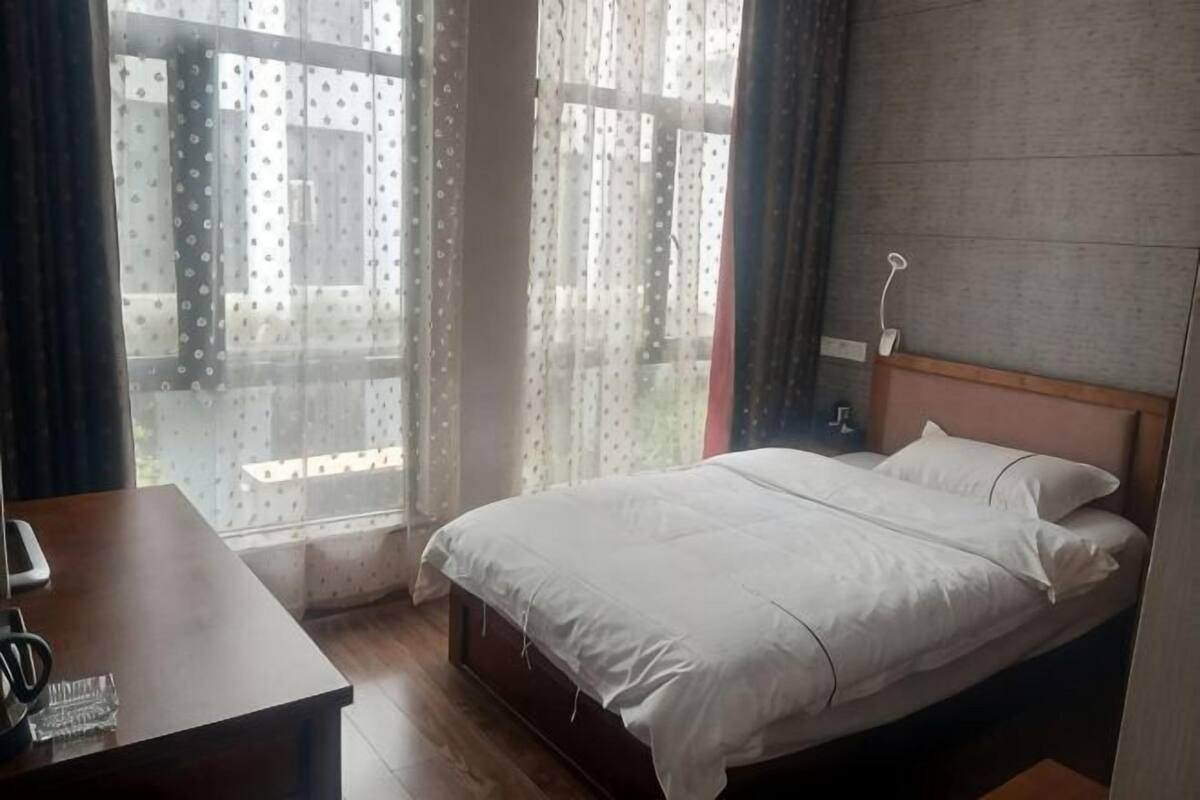 A bedroom with a bed, a bedside table, a lamp, and a window with curtains.