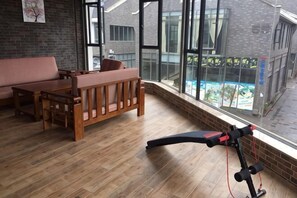 Quarto com piso de madeira, um banco, uma mesa e janela com vista para prédios e varanda.