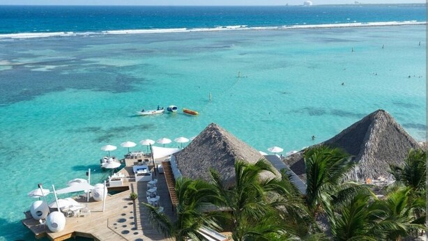 An aerial view of a beachside resort with clear turquoise waters, a lounge area with umbrellas, and thatched-roof structures. - Hotel Boca del Mar Playa Boca Chica Penthouse (Boca Chica)