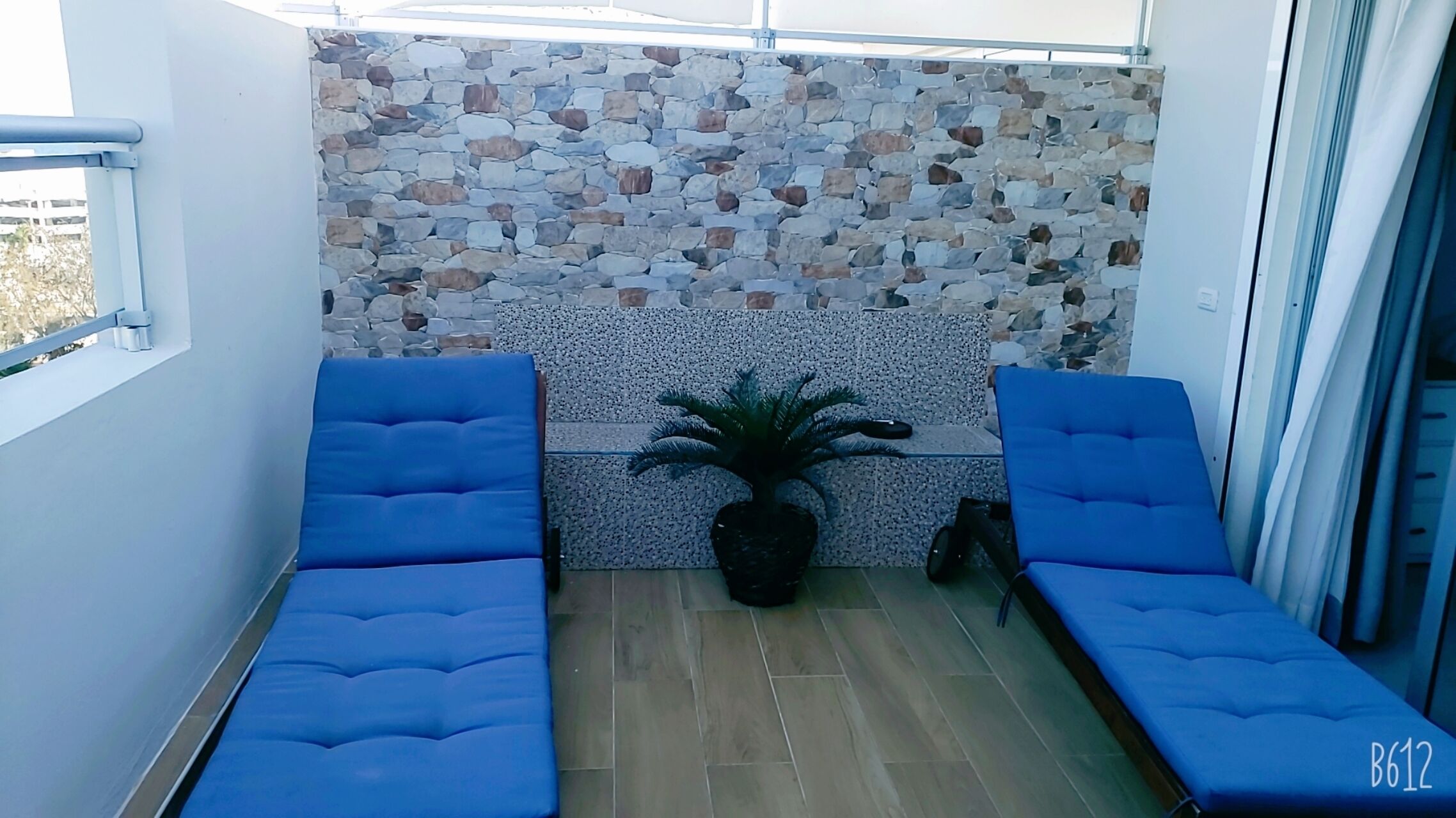 Un balcon avec deux chaises bleues dotées de coussins, un mur en pierre et une plante en pot.