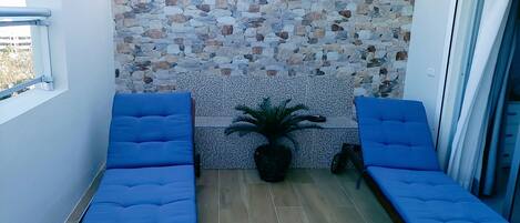 Un balcon avec deux chaises bleues dotées de coussins, un mur en pierre et une plante en pot.