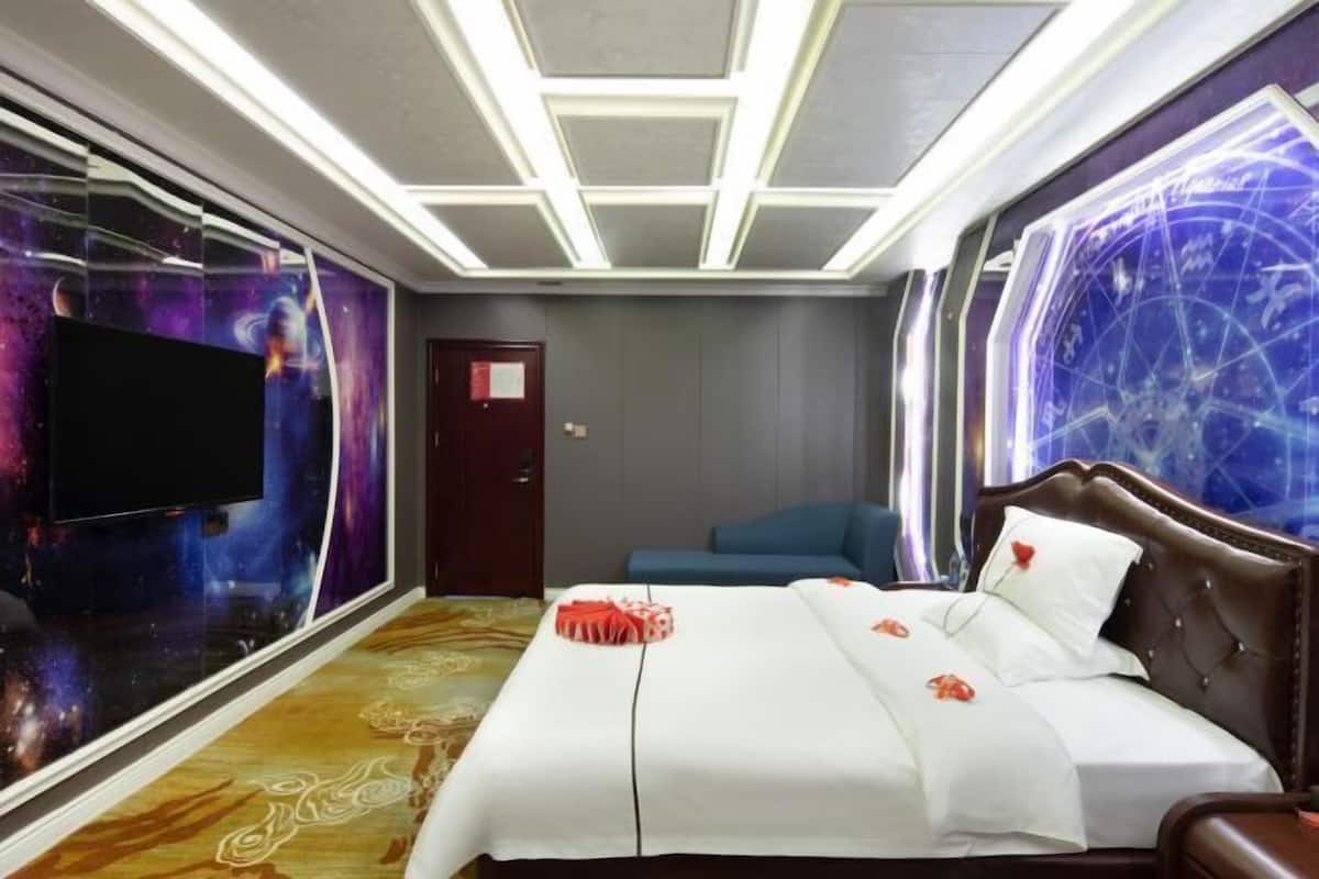 Habitación de hotel con una cama grande, un televisor de pantalla plana, un mural en la pared y un techo con diseño geométrico.