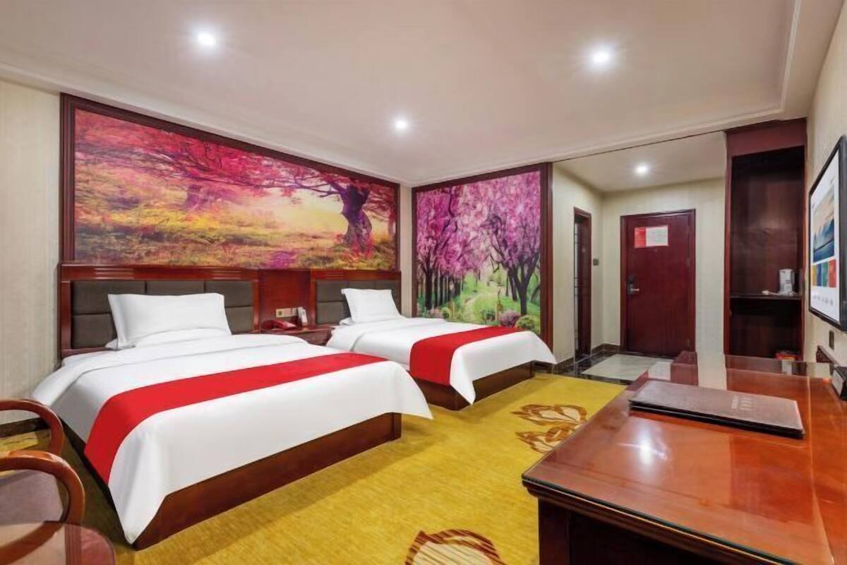 Una habitación de hotel con dos camas, un escritorio de madera y grandes cuadros en las paredes.