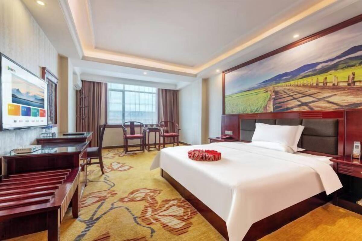 Una habitación de hotel con cama, escritorio, sillas, un cuadro y ventana.