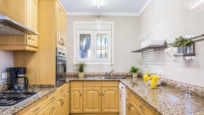 A kitchen with wooden cabinets, a built-in stove, a coffee maker, a sink, and a window with a view of palm trees. - Villa Mila - Five Bedroom Villa, Sleeps 10 (Calp)