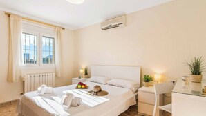 A neatly arranged hotel room with a bed, a bedside table with a lamp, a chair, a small desk, and a window with curtains. - Villa Mila - Five Bedroom Villa, Sleeps 10 (Calp)