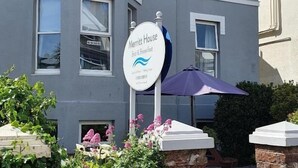 A two-story building with a sign for 'Merritt House Bed & Breakfast' and a purple umbrella.