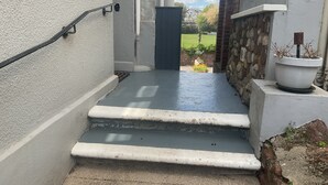 A concrete staircase leading to a door, with a stone wall and a potted plant on the right.