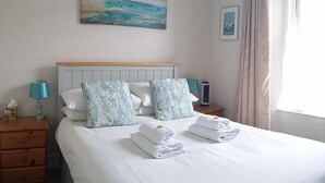 A hotel room with a bed, two bedside tables, a lamp, a picture on the wall, and a window with curtains.
