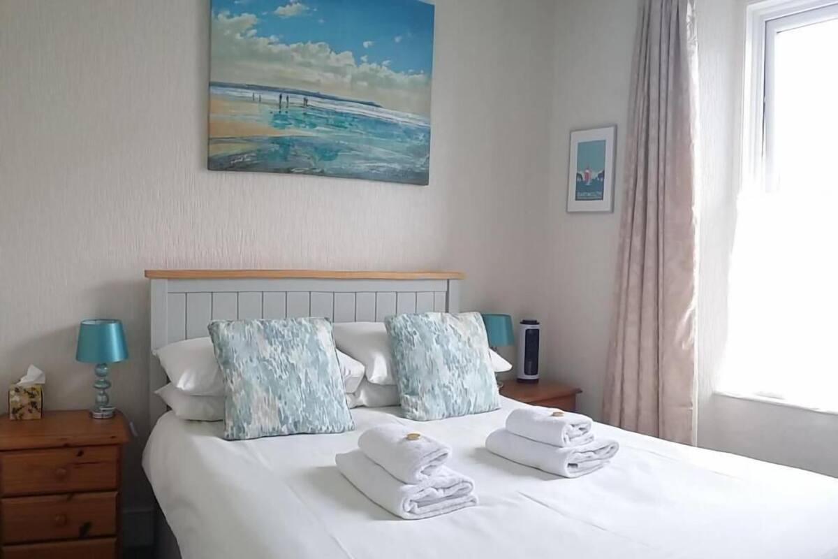 A hotel room with a bed, two bedside tables, a lamp, a picture on the wall, and a window with curtains.