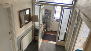 A hallway with a radiator, a mirror, a lamp, and a door leading to a room with a bulletin board and a window.