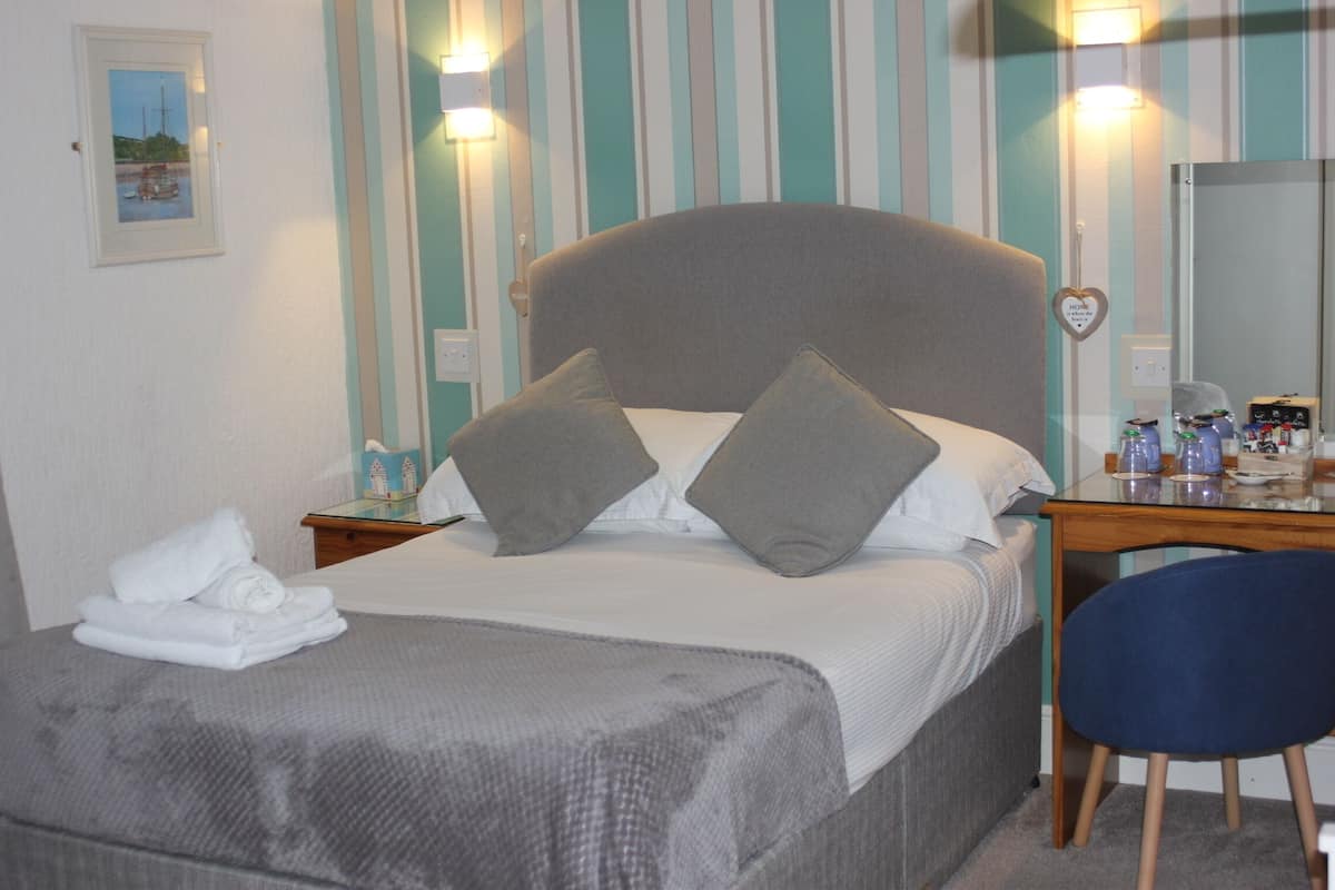 A bed with pillows, a bedside table with toiletries, a chair, and a wall with striped wallpaper.
