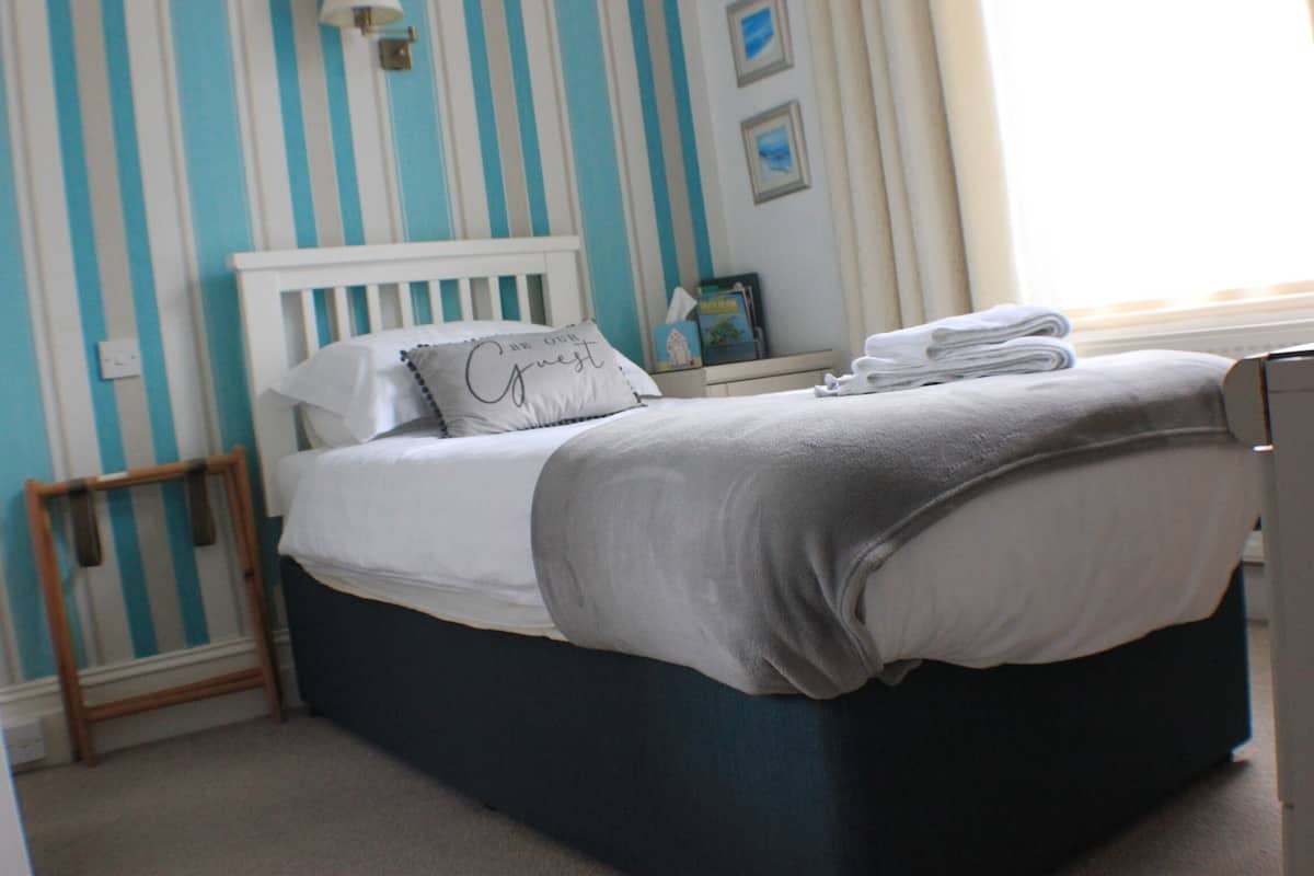 A bed with a white headboard, a grey blanket, and a pillow with text.