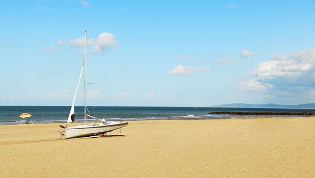 Ein Segelboot an einem sandigen Strand unter blauem Himmel.