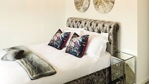 Ein Schlafzimmer mit einer gepolsterten Kopfteil, einem Bett mit weißer Bettwäsche, zwei dekorativen Tellern an der Wand und einem Nachttisch mit Schubladen.