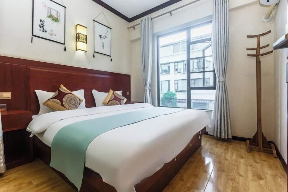 Ein Hotelzimmer mit einem großen Bett, einem Holzkopfstück und Blick auf Gebäude durch das Fenster.