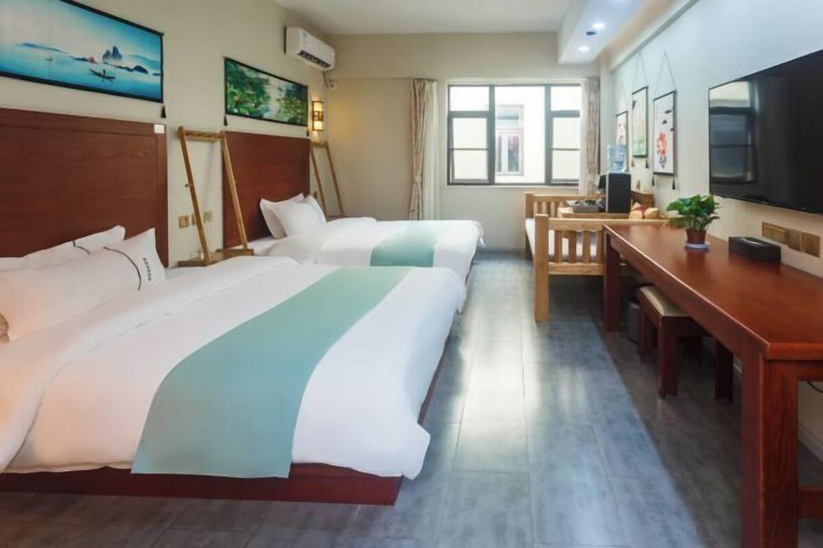 Ein Hotelzimmer mit zwei Betten, einem Schreibtisch, einem Sessel, einem Fernseher und Bildern an den Wänden.