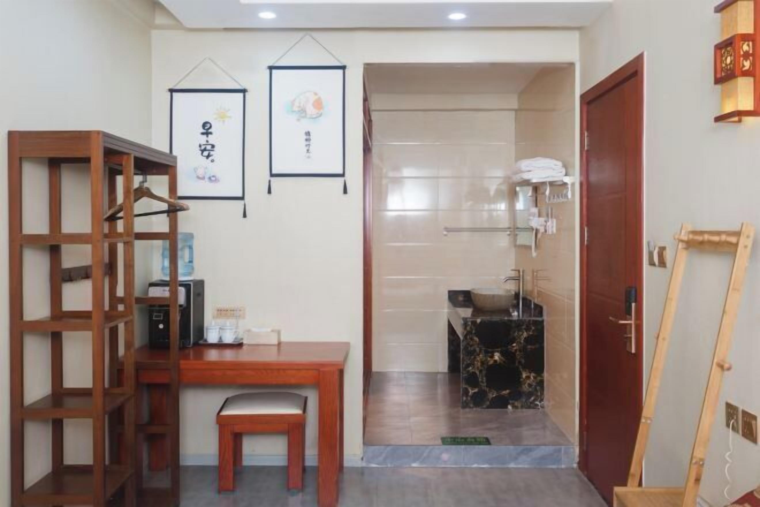A room with a wooden desk, a chair, a hanging picture frame, a bathroom with a sink and towel rack, and a wooden ladder.