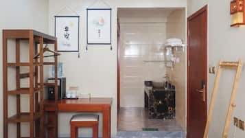 A room with a wooden desk, a chair, a hanging picture frame, a bathroom with a sink and towel rack, and a wooden ladder.