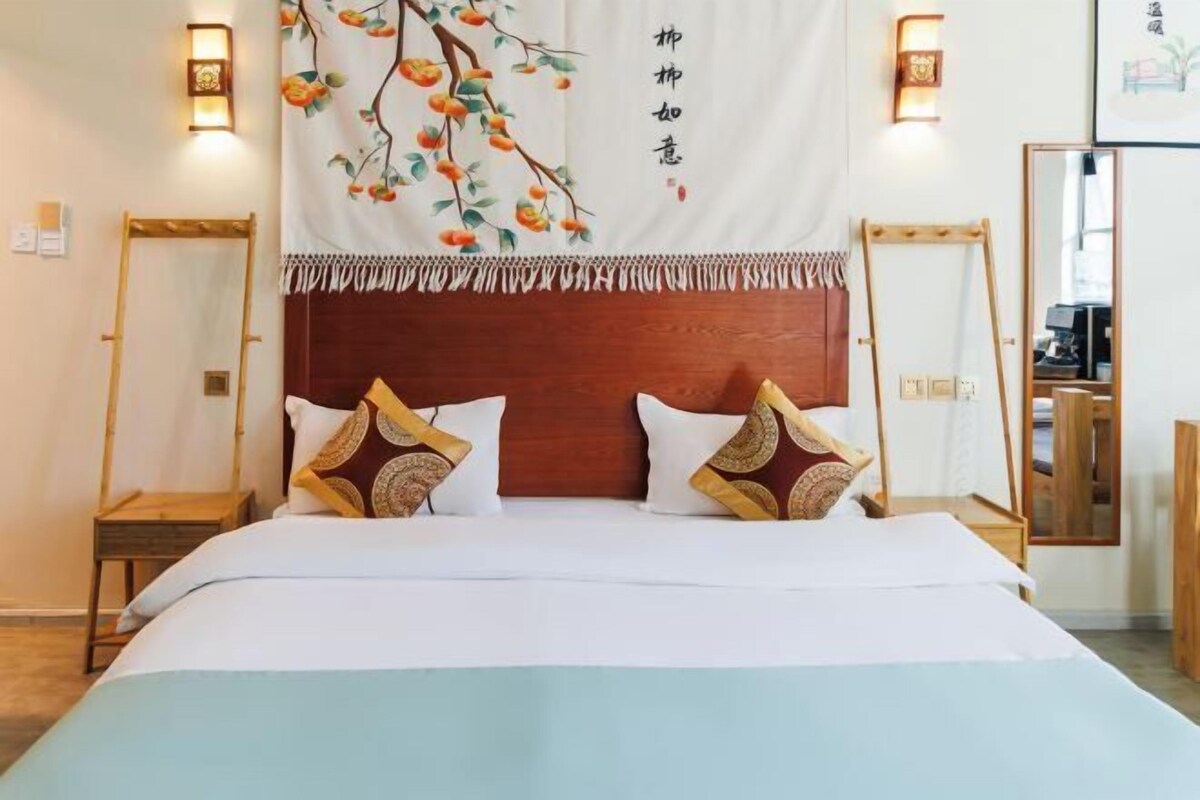 A hotel room with a bed, two bedside tables, a mirror, and a wall-mounted light fixture.