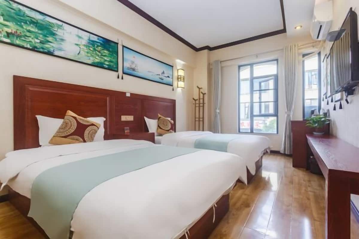 Ein Hotelzimmer mit zwei Betten, Holz-Kopfteilen und einem großen Fenster mit Vorhängen.