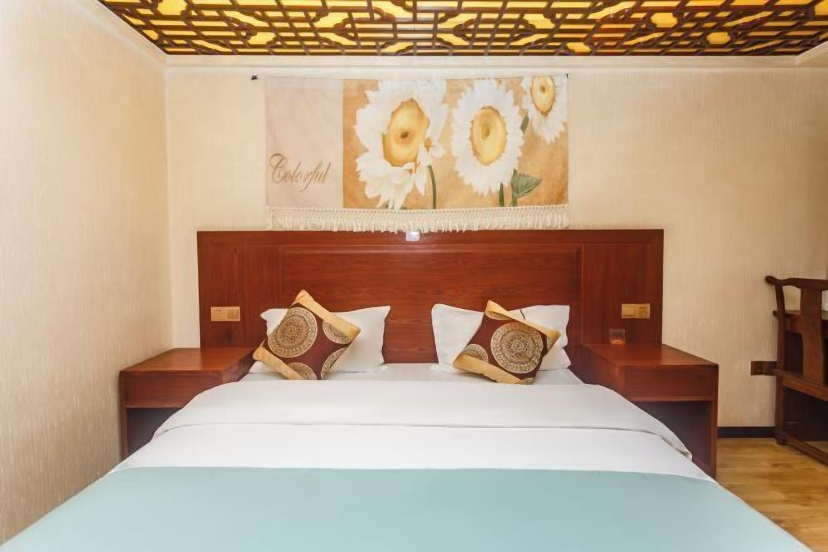 Un dormitorio con cabecera de madera, dos mesitas de noche, una cama con ropa de cama blanca y un cuadro de girasol en la pared.
