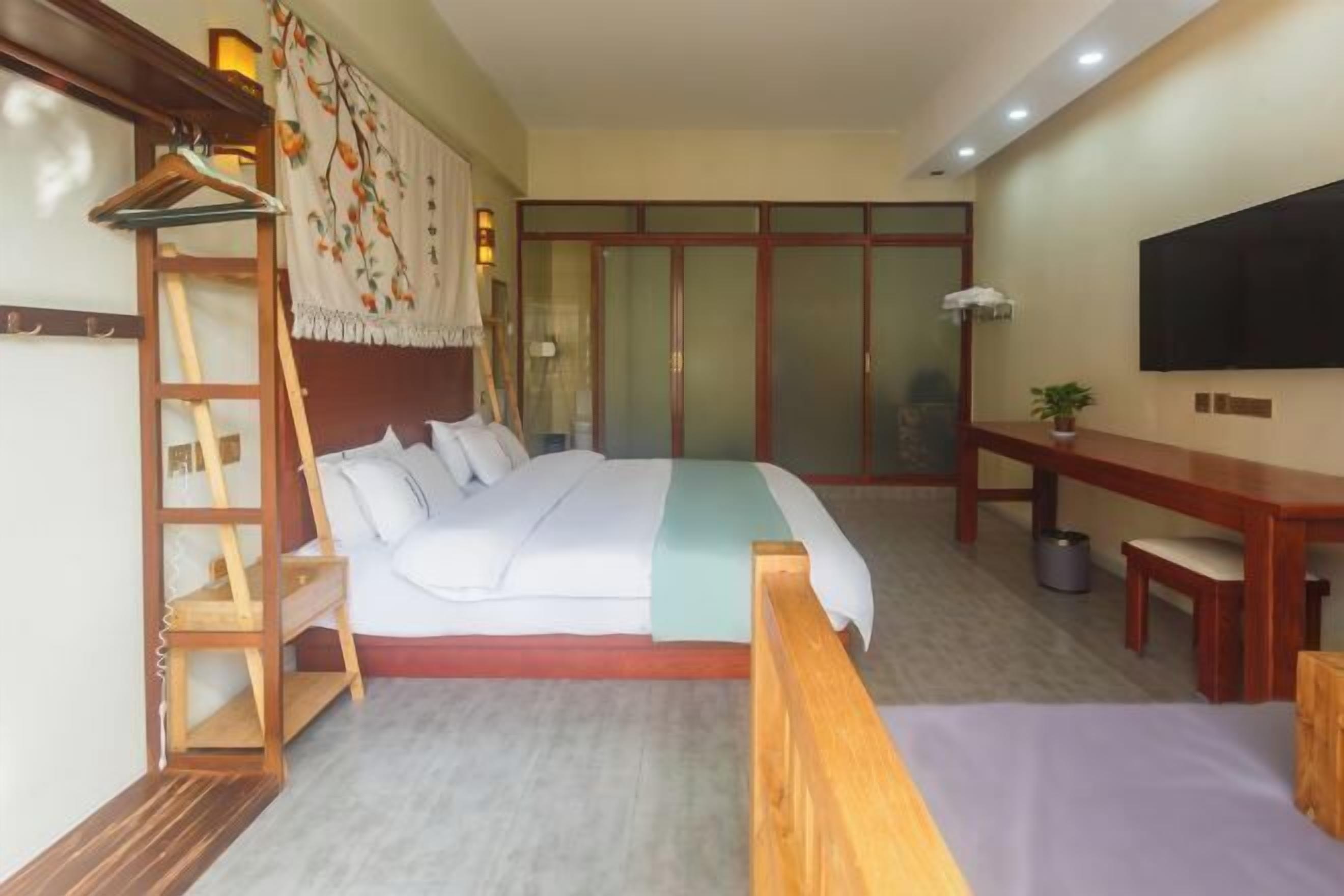 A bedroom with a bed, wooden furniture, a desk, and a TV.