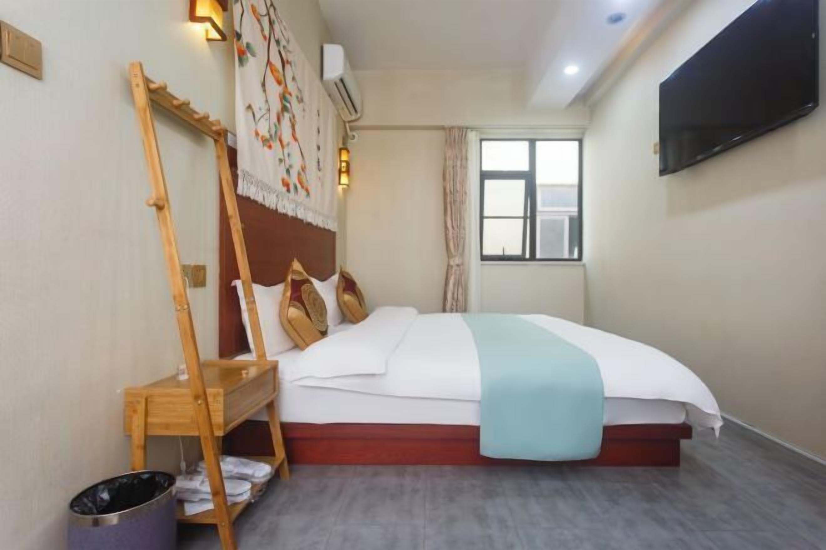 A hotel room with a bed, a wooden ladder, a wall-mounted TV, and a window with curtains.