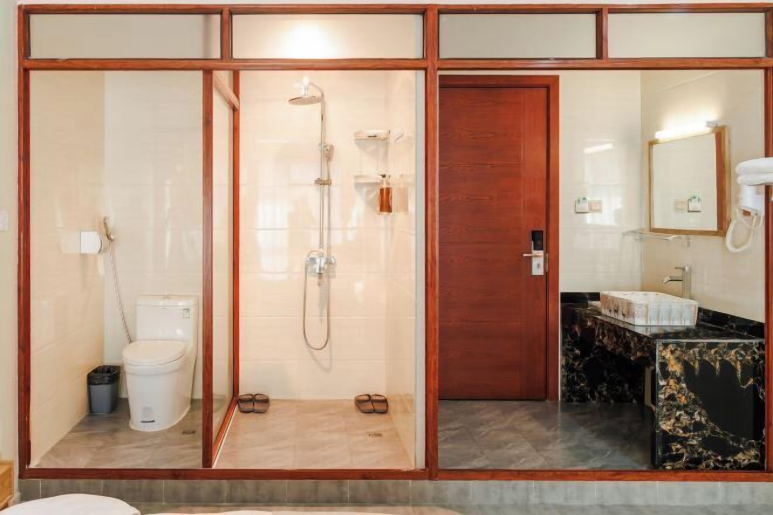 A bathroom with a glass-enclosed shower, a toilet, a sink with a marble countertop, and a wooden door.