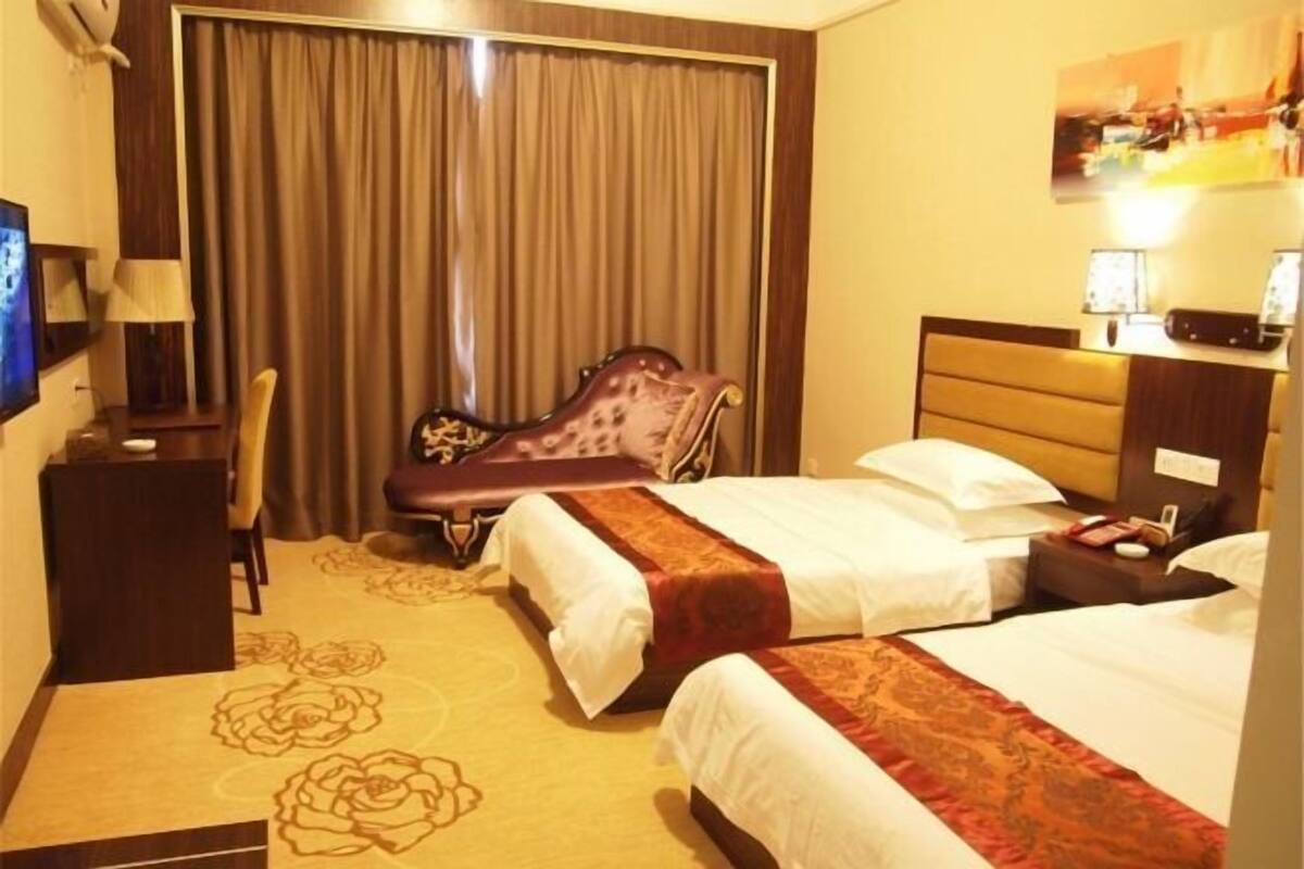 A hotel room with two beds, a desk, a chair, a TV, and a curtain.
