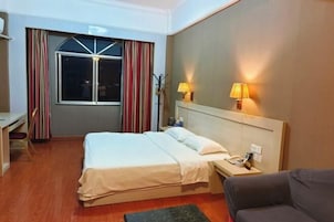 Una habitación de hotel con cama, mesita de noche, lámpara y ventana con cortinas.