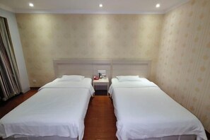 A hotel room with two single beds, a nightstand, and a mirror above the bed.