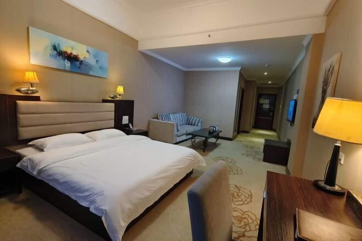A hotel room with a large bed, a sofa, a small table, and a TV.