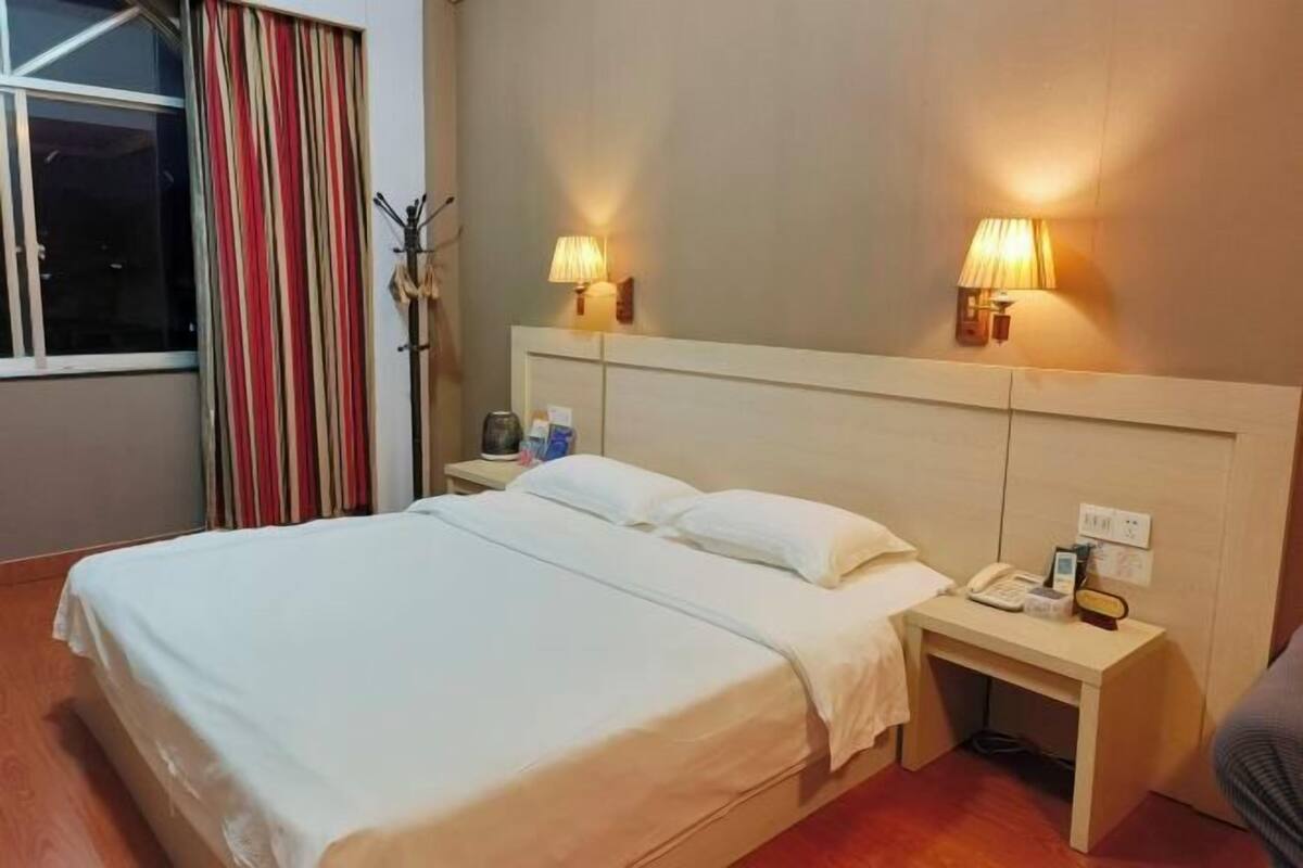 A hotel room with a bed, bedside lamps, a nightstand, and a window with curtains.