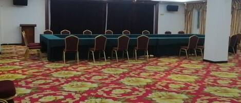 A conference room with a long table and chairs, a patterned carpet, and a stage area.