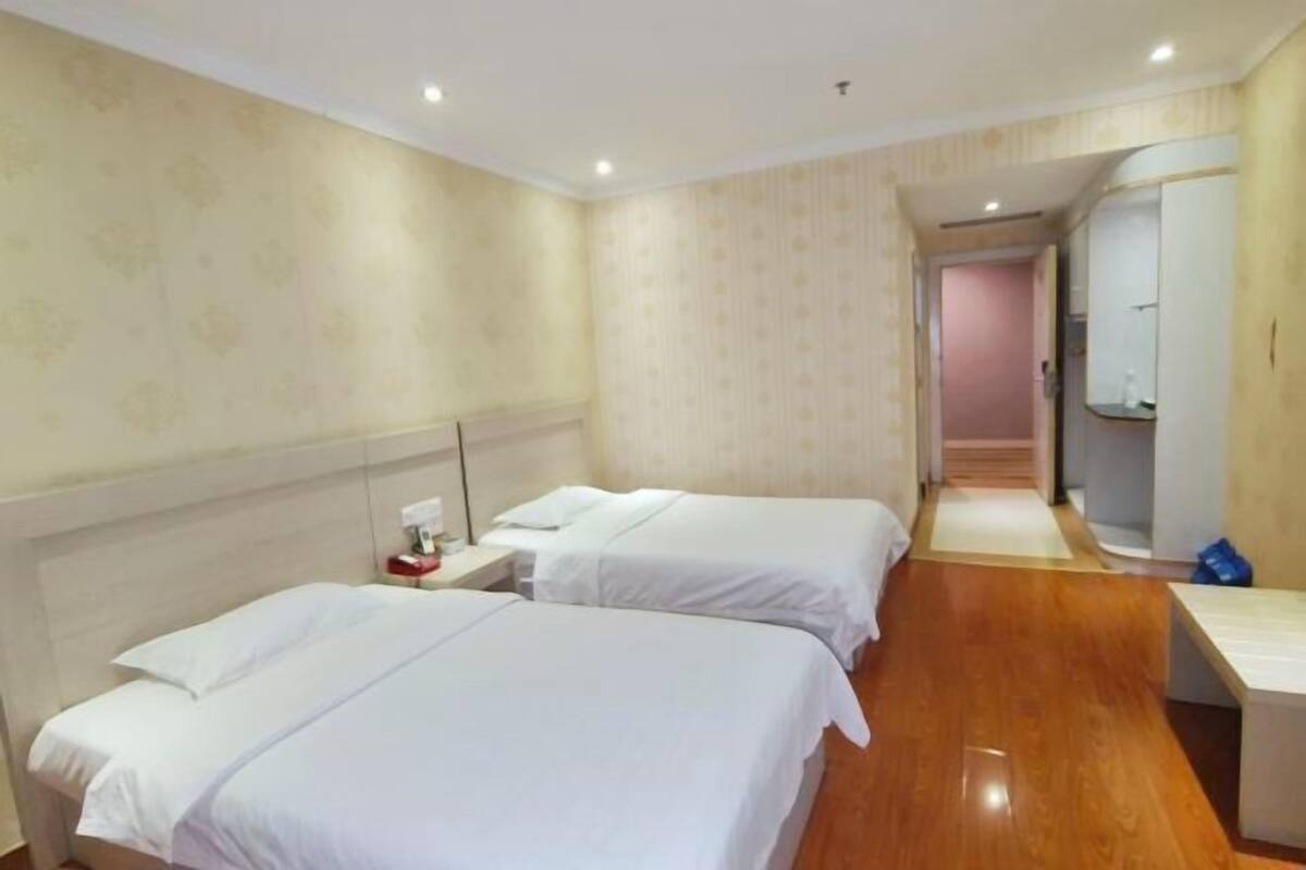 A hotel room with two beds, a nightstand, a mirror, and a wooden floor.