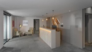 Un espace d’accueil moderne comprenant un comptoir de réception, deux chaises, une petite table et une œuvre d’art accrochée au mur.
