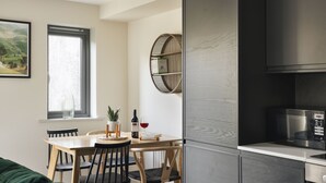 Une cuisine moderne dotée d’un four à micro-ondes et d’un four encastrés, un coin repas avec des chaises et une table en bois, et une fenêtre offrant une vue sur la campagne.