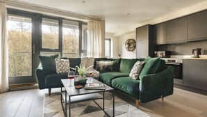 Un salon moderne avec un canapé vert, une table basse et une cuisine en arrière-plan.
