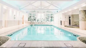 Une piscine intérieure à l’eau claire, entourée de murs et surmontée d’un plafond au motif géométrique.