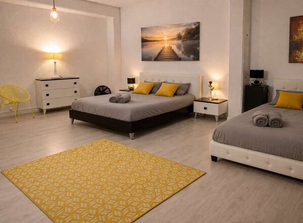 A modern bedroom with two beds, a yellow patterned rug, and a painting of a sunset over a lake.