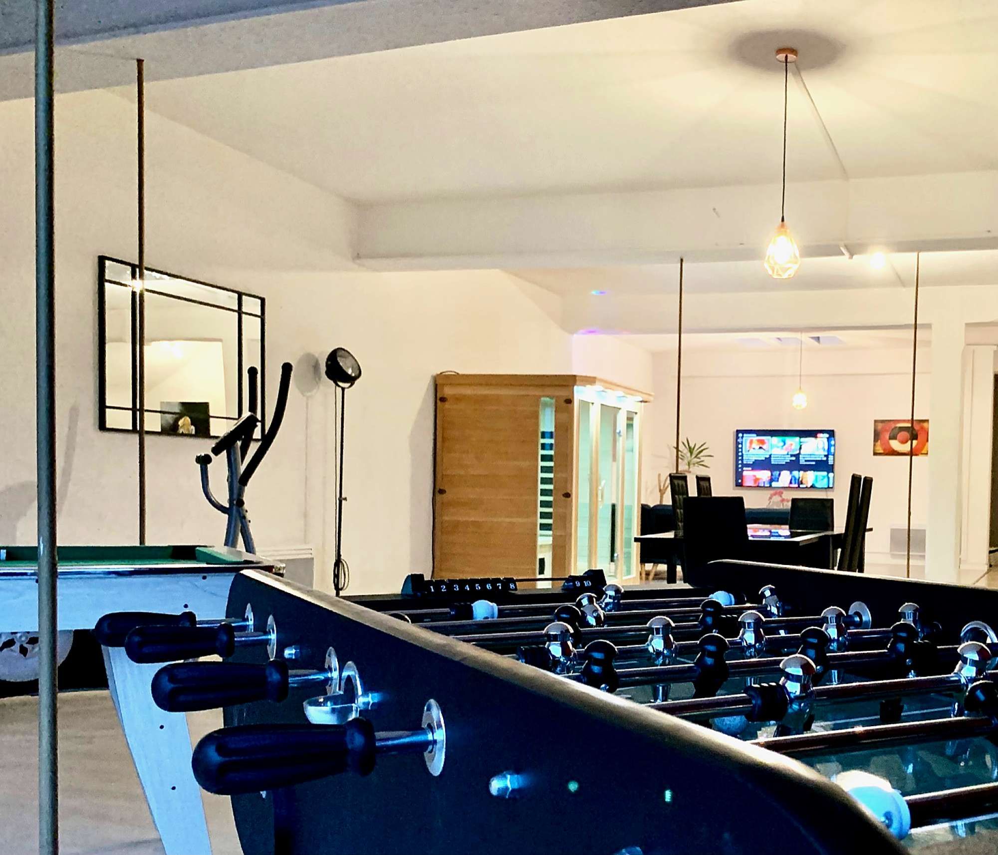 A foosball table in a room with a television, a mirror, and a wooden cabinet.