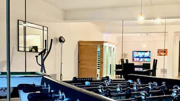 A foosball table in a room with a television, a mirror, and a wooden cabinet.