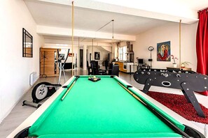 A pool table in a room with a dining area, exercise equipment, and a painting on the wall.