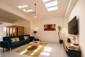 A modern living room with a sofa, coffee table, artwork, and a TV. - Loft Cosy - Hypercentre - Sauna - 200m2 - Wifi (Graulhet)