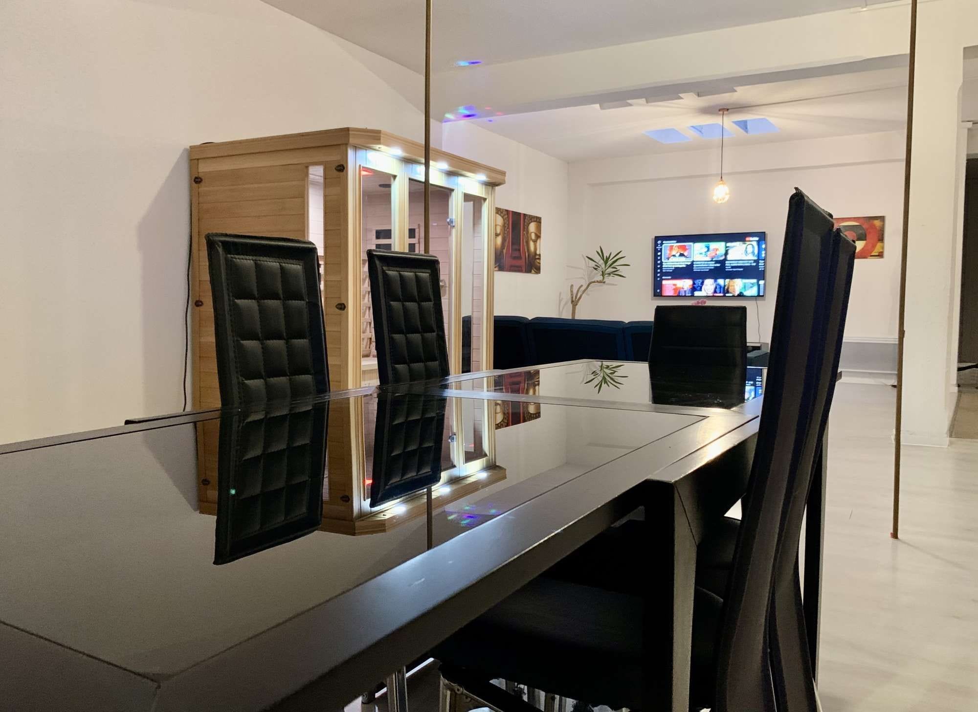 A modern dining area with a glass table, black cushioned chairs, and a wooden accent piece.