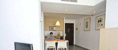 Ett modernt kök med vita skåp, en mikrovågsugn och en matplats med två vita stolar.